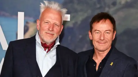 Author Raynor Winn defends herself against claims she misled readers Getty Images Moth Winn (L) and Jason Isaacs attend the UK special screening of The Salt Path at The Curzon Soho in London. Winn is wearing a dark suit, white shirt and a red and white spotty cravat. Isaacs is wearing a black suit and open-neck shift.