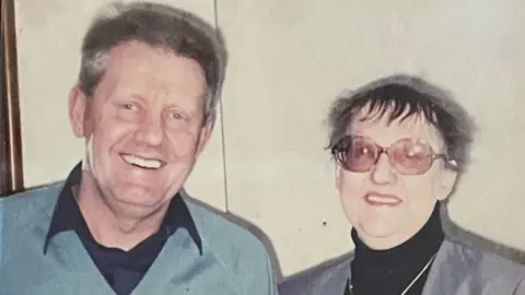 Canterbury sub-postmistress conviction referred to appeal court Handout Two people in an old photo - on the left is a man with brown hair in a blue jumper and black shirt. On the right is Patricia, a woman with a black roll neck, a grey blazer and glasses.