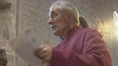 Police investigate sex abuse claims against men linked to Church A white-haired man with a purple robe inside a church holding a piece of paper is speaking