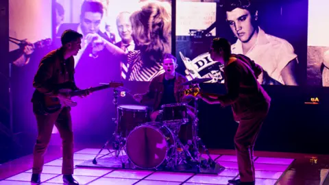 'Atrocious and misleading' show upsets some fans Graham Turner Three men on stage playing instruments as pictures of Elvis appear in the background