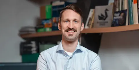 Space technology: Lithuania's promising space start-ups BlackSwan Space Tomas Malinauskas with a moustache and in front of bookshelves.