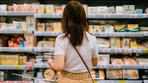 Food prices remain 'stubbornly high' in Northern Ireland as inflation rate rises Getty Images A young woman carrying shopping basket, choosing cheese, standing in front of produce aisle in a supermarket. She has long brown hair and is wearing a grey top with beige trousers.