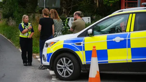 Child dies and 21 injured as Minehead school coach overturns PA Media A female police officer in uniform talks to local residents standing next to a police car in Wheddon Cross in Somerset after a coach crash