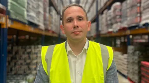 Food prices remain 'stubbornly high' in Northern Ireland as inflation rate rises BBC Mr Gamble is standing in a warehouse. He's wearing a yellow high-viz jacket. Behind him are shelves stacked with goods.