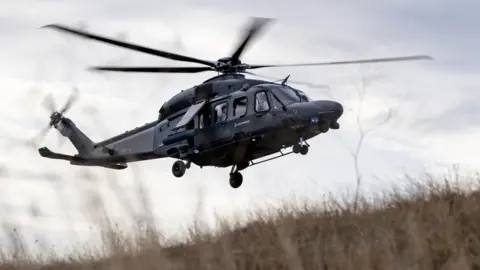 Defence firms 'confident' hundreds more jobs will come Leonardo Helicopters A helicopter flying. It is black. The camera is looking up. Grass on the floor is blowing from the rotors.