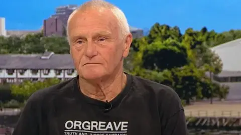 Battle of Orgreave national inquiry confirmed by Yvette Cooper John Dunn, who has short, shaved grey hair and blue eyes. He is wearing a black t-shirt which reads 'ORGREAVE TRUTH AND JUSTICE CAMPAIGN'.