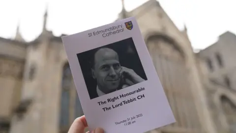 Funeral held for Norman Tebbit at Bury St Edmunds cathedral PA Media An order of service is held up in front of St Edmundsbury Cathedral, it has a black and white image of Lord Tebbit and details of the date and timings of the funeral service.