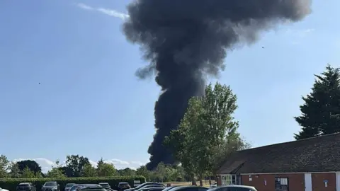 Southend Airport plane crash: Flights cancelled after incident Frazer Brooks Thick dark smoke is billowing into the blue sky from the incident - which cannot be seen in the image.