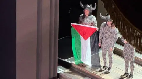 Performer launches Gaza flag protest on Royal Opera House stage Magdalini Liousa A performer dressed in a military costume with Viking horns holds a large Palestine flag on a stage at the Royal Opera House