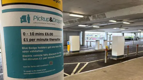 Airport drivers try to beat drop-off charges by parking in laybys A sign displaying the pickup and drop-off charges at Edinburgh Airport. The text is white on a teal blue background. Above it is a white box with black writing which reads: 0-10 mins £6. £1 per minute thereafter.