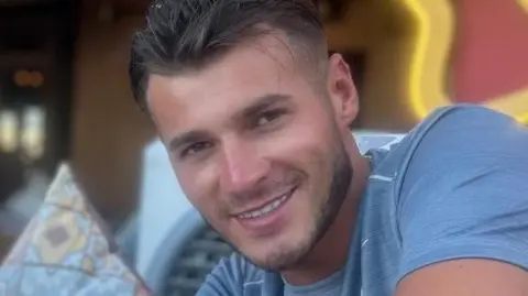 Met Police blue stevens, man in blue t-shirt smiling at the camera. He has short brown hair and slight stubble.