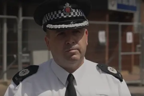 Officers attacked at Epping asylum hotel protest, police say Assistant Chief Constable Stuart Hooper in uniform. He is standing outside. There is metal fencing round a building behind him.