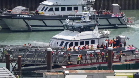 Small boats crossings hit 25,000 for the year PA Media A group of people thought to be migrants are brought in to the Border Force compound in Dover, Kent, from two Border Force vessels following a small boat incident in the Channel.