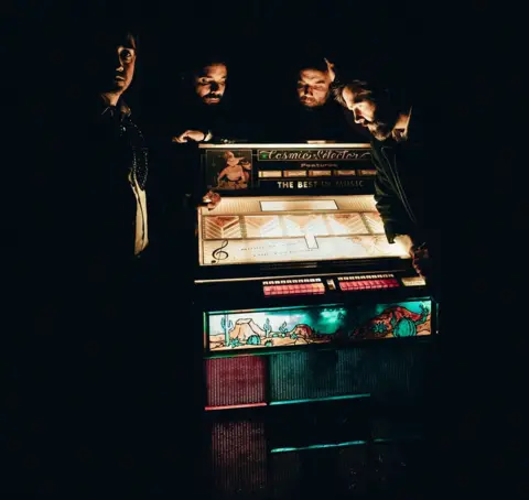 The 10-year-old song that keeps getting bigger Cole Silberman Four band members standing in semi-darkness around an old-fashioned lit-up jukebox with "The Cosmic Selector" written in decorative lettering on the top