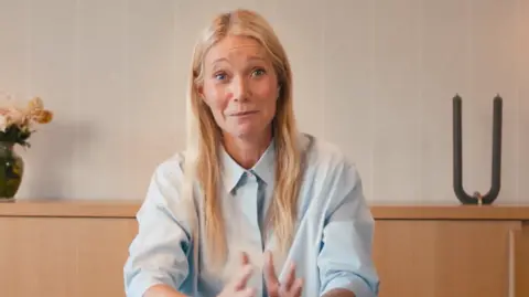 Astronomer's 'clever' PR move embracing CEO scandal Astronomer Gwyneth Paltrow appearing in a promotional video for Astronomer. Behind her is a wooden shelf with a plant and a candle on top of it. She is wearing a light blue shirt.