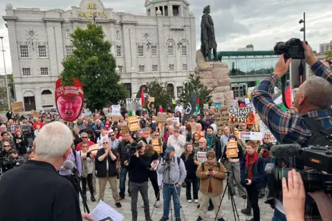 Security tightens as Donald Trump plays golf at Turnberry Several hundred anti-Trump protesters with placards in Aberdeen - journalists at the right of the frame point cameras at the crowd