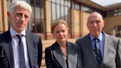Health professionals failed Graham Thorpe, coroner says Briony Leyland/BBC A man in a black suit and tie, standing next to a woman in a dark suit and she is standing next to another man wearing a dark grey suit. They are standing in front of Surrey Coroner's Court.