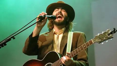 The 10-year-old song that keeps getting bigger Getty Images Ben Schneider in a brown suit and hat holding a guitar and singing into a microphone on stage