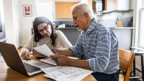 OBR says pension triple lock to cost three times initial estimate Getty Images Older man and woman sit at a kitchen table with paperwork and a laptop in front of them