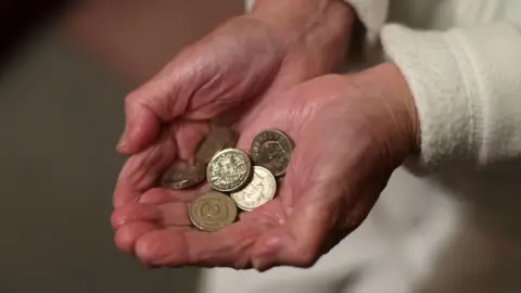 PA Media An old person holding some pound coins.