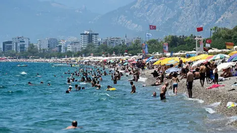 Package holidays to Spain, Cyprus and Turkey soar in price Getty Images A beach in Turkey where lots of people are sunbathing under umbrellas, and many other people are swimming in the sea