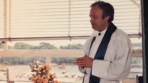 Police investigate sex abuse claims against men linked to Church D J Photography A younger Anthony Pierce stands clasping his hands with his back to a window. He is side of frame and is wearing white robes with a dark silk stole around his neck.