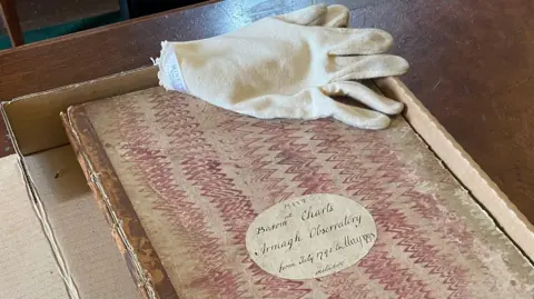 230 years of unbroken weather recordings BBC A close-up of a very old book containing records of weather observations from Armagh Observatory from July 1795 to May 1798. The book, which has a hand-written cover and is decorated with wavy red lines, is in a cardboard box on a wooden desk. A white glove used for handling the delicate paper is lying on the book.