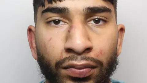 Man guilty of Manchester Airport attack on police officers Greater Manchester Police A mugshot of a young man with short dark hair and a dark beard. His face is covered in red scratches and bruising.