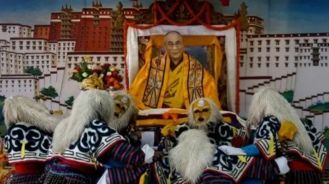 Thousands turn out to celebrate Dalai Lama's 90th birthday Reuters Tibetans in yellow masks and with white fluffy headdresses on, in colourful long-sleeve outfits perform a traditional mask dance in front of a cut-out of the Dalai Lama wearing all orange and yellow atop a throne
