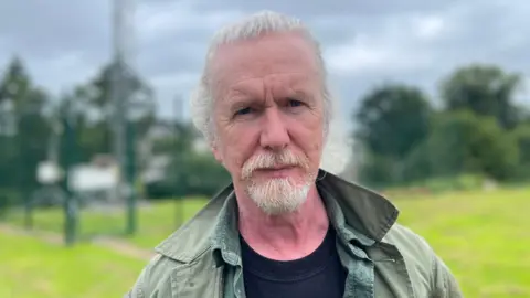 230 years of unbroken weather recordings Shane Kelly, a man with white hair and beard, looks into the camera. He is wearing a green coat over a black t-shirt and a green shirt.