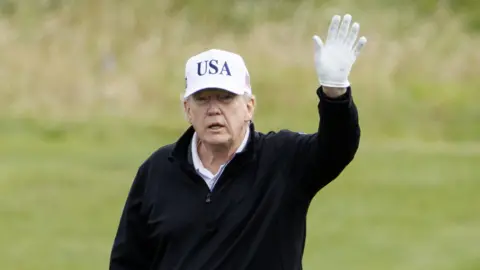 Trump back on the golf course for day two of Scottish visit EPA Donald Trump waves a white-gloved hand as he walks on his Turnberry golf course. He is waring a black jumper and a white USA hat