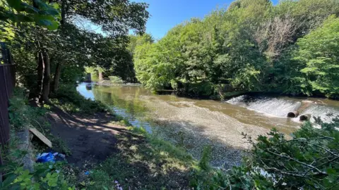 Boy, 15, dies in river incident in Glasgow on hottest day BBC A river surrounded by trees with a blue sky behind it. There is a little dip in the river where water rushes down the a lower level. Two pipes stick out of the hill.