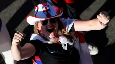 How England fans are preparing for the Euro 2025 final Reuters An England fan wearing sunglasses, a red and white England cowboy hat with a flag tied around their neck looks up into the camera punching their arms in the air in celebration.