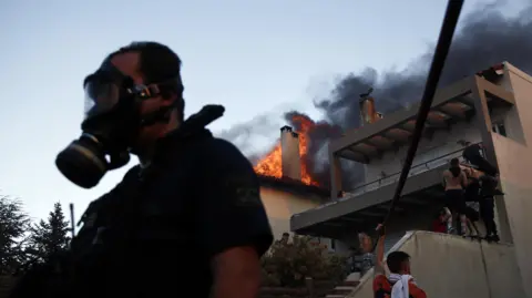 Greece battles wildfires, evacuating residents near Athens YANNIS KOLESIDIS/EPA/Shutterstock Volunteers battle to put out a fire burning houses in the residential area of Kryoneri, in the suburbs of Athens, Greece