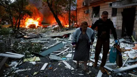 Reuters A woman receives assistance as she leaves the apartment building hit during Russian missile and drone strikes in Kyiv, Ukraine early on Thursday