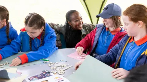 Girlguiding unveils 72 new badges including 'fandoms' and 'laughter' Girlguiding Girls doing an activity involving tiles and paper.