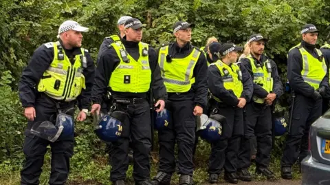 Epping council votes to urge government to shut asylum hotel Nadira Tudor/BBC A row of police officer with their helmets attached to their belts are stood together on a public street.