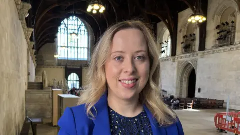 Latin makeup labels put allergy sufferers at risk, say campaigners Becky Gittins, who has wavy blonde hair and is wearing a blue suit jacket with a blue animal print dress, smiles at the camera