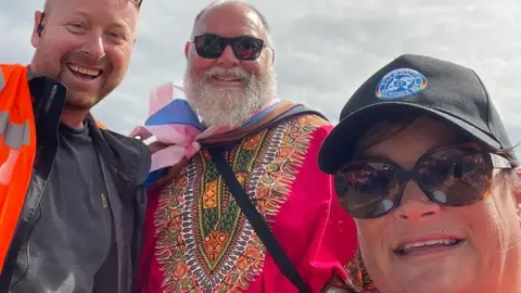 London Pride returns as events struggle with falling funds Alex MacDonald Alex is pictured with two other volunteers outside at a previous Plymouth Pride event. All three are smiling at the camera, while Alex wears an orange hi-vis jacket over a dark top.