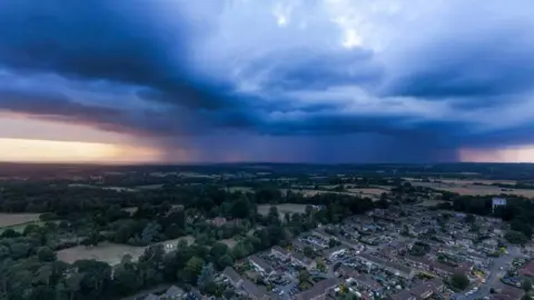 Yellow warnings as thunderstorms could bring flash floods Chris Partridge A moody dark cloudy sky over countryside fields and houses, taken from above via a drone.