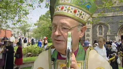 Police investigate sex abuse claims against men linked to Church Former Bishop of Swansea and Brecon Anthony Pierce is a grey-haired man wearing thin-rimmed rectangular glasses. He is wearing a purple shirt with a dog collar and has green, white and gold robes.