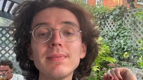 Bangor Cathedral had 'binge drinking culture' at diocese Esme Byrd A picture of a person's face with brown wavy hair and circular glasses with a garden trellis behind and trees climbing up it