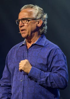 A gray-haired man wearing glasses and a blue shirt.