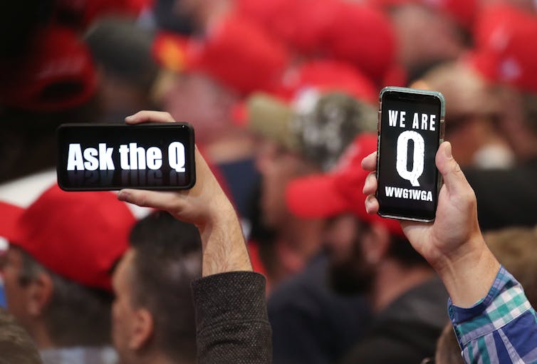 How the QAnon movement entered mainstream politics – and why the silence on Epstein files matters Two people holding up cellphones with messages 'Ask the Q' and 'We are the Q.'
