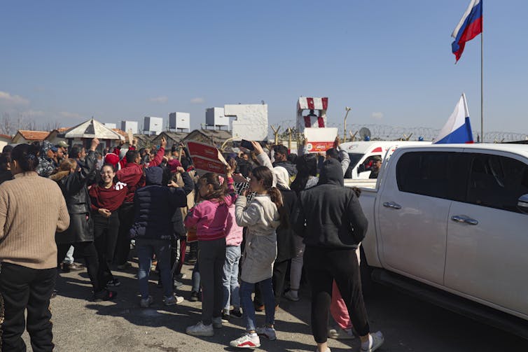 Understanding the violence against Alawites and Druze in Syria after Assad Several people, including women and children, stand next to parked vehicles.