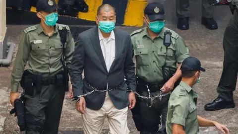 Who is Jimmy Lai, the HK media tycoon on trial for national security crimes? Reuters Lai, dressed in a gray suit and beige pants, walks handcuffed and flanked by three police officers to a police van
