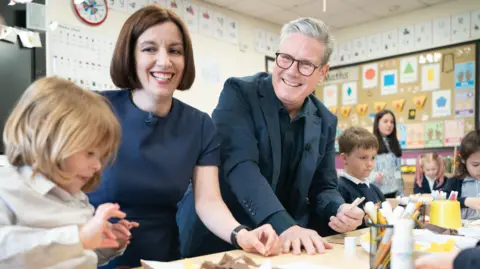 How can working parents get 30 hours of free childcare? PA Media Education Secretary Bridget Phillipson is pictured with Prime Minister Sir Keir Starmer during a visit to Nursery Hill Primary School, in Nuneaton, Warwickshire before the 2024 general election. They are smiling and are surrounded by children who are doing crafts.