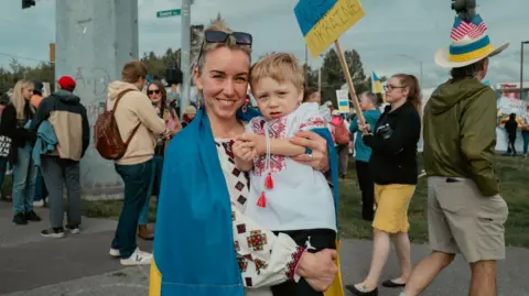 Alaskans share anger and hope as Trump and Putin fly in BBC A woman with blonde hair in a Ukrainian flag holds a a boy in her arms