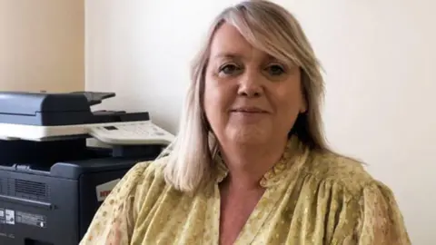 Free school uniform schemes demand is rising Wolverhampton City Credit Union A woman with blonde hair and a yellow top in an office with white walls and a black printer behind her