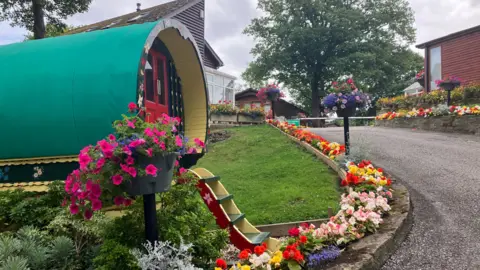 Holidays with grandparents 'on the up' amid summer childcare cost A recreation of an old gypsy caravan sits at the entrance to the caravan park. There are colourful flower beds leading up the roadside from the main entrance